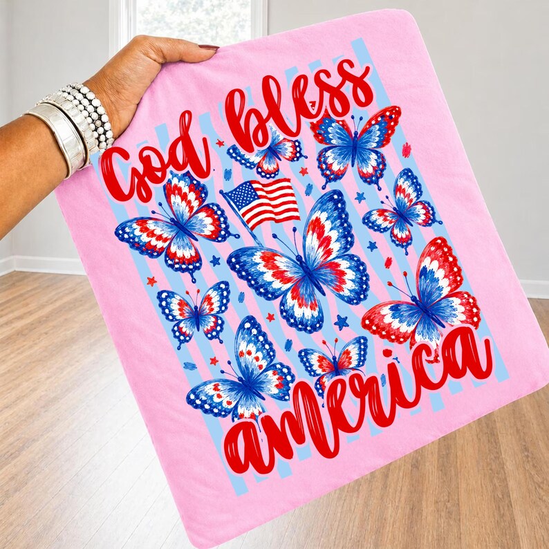 May include: A light pink square fabric item featuring a graphic print of red, white, and blue butterflies, a small American flag, and the red script text God bless America. The design includes light blue vertical stripes and small red stars.
