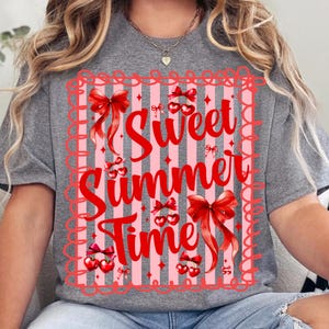 Pu&ograve; includere: Una maglietta grigia con un design rosso e rosa. Il design presenta il testo "Sweet Summer Time" in corsivo rosso, circondato da fiocchi rossi, ciliegie e uno sfondo a righe rosa.