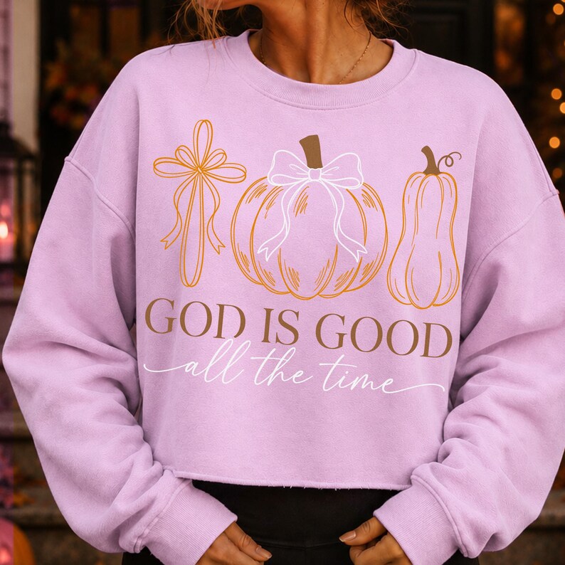 Puede incluir: Una sudadera de manga larga color morado claro con un estampado gr&aacute;fico de una cruz con un lazo, una calabaza con un lazo y una calabaza alargada. El texto dice "GOD IS GOOD" en letras marrones y "all the time" en cursiva blanca debajo.
