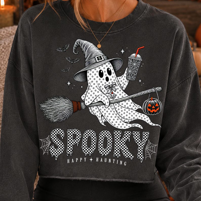 May include: A charcoal grey long-sleeve sweatshirt featuring a graphic of a ghost wearing a witch hat, riding a broomstick, and holding a drink. The ghost is decorated with stars and a pumpkin. The text reads SPOOKY HAPPY HAUNTING in a checkered font.