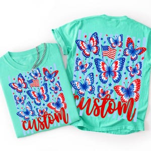 Peut inclure: Un t-shirt vert menthe avec un imprim&eacute; graphique de papillons rouges, blancs et bleus, un petit drapeau am&eacute;ricain et le mot custom en &eacute;criture rouge. Le motif comprend des rayures verticales bleu clair et de petites &eacute;toiles rouges et bleues.