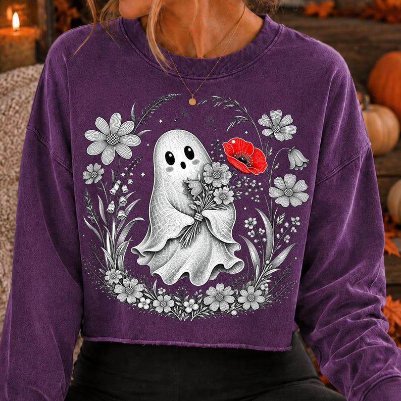 K&ouml;nnte beinhalten: Ein violettes Langarm-Sweatshirt mit Rundhalsausschnitt und einer Grafik eines wei&szlig;en Geistes, der einen Blumenstrau&szlig; h&auml;lt. Das Design zeigt schwarz-wei&szlig;e Strichzeichnungen von Blumen um den Geist herum, mit einer einzelnen roten Mohnblume.