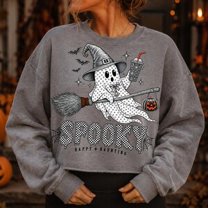 May include: A grey long-sleeve sweatshirt featuring a graphic of a ghost wearing a witch hat, holding a drink and a broomstick with a hanging jack-o'-lantern. The text reads SPOOKY and HAPPY HAUNTING, accompanied by small bats and spiderwebs.