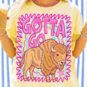 May include: Yellow t-shirt with a pink and blue graphic that says "GOTTA GO" above a cartoon bison. The bison is tan with horns and is surrounded by stars and a pink border.