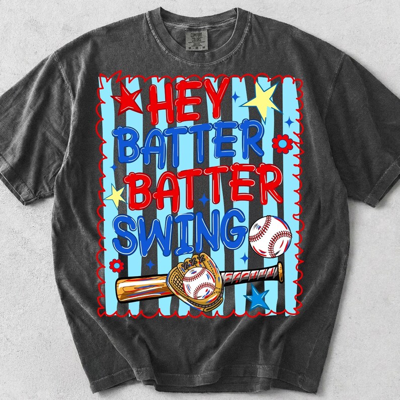K&ouml;nnte beinhalten: Dunkelgraues T-Shirt mit Baseball-Motiv. Das Design zeigt den Text "HEY BATTER BATTER SWING" in Rot und Blau, sowie einen Baseball, Schl&auml;ger und Handschuh. Sterne und Blumen erg&auml;nzen das Design.