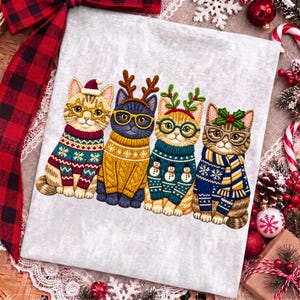 May include: A light gray fabric featuring an embroidered design of four cats sitting in a row. Each cat wears glasses and a colorful winter sweater. The cats are adorned with festive accessories including a Santa hat, reindeer antlers, and holly.