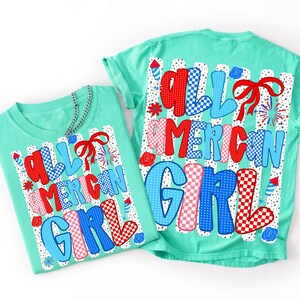 Pode incluir: Duas camisetas verde-menta com o texto "ALL AMERICAN GIRL" em vermelho, branco e azul. As letras t&ecirc;m padr&otilde;es xadrez e bolinhas. O design inclui fogos de artif&iacute;cio, la&ccedil;os e detalhes florais.