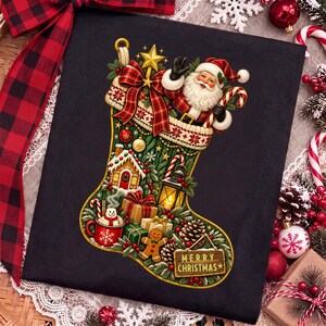 Może przedstawiać: Czarny t-shirt z dużą grafiką zielonej świątecznej skarpety wypełnionej bożonarodzeniowymi motywami, takimi jak postać Świętego Mikołaja, domek z piernika, latarnia, prezenty, bałwan w kubku oraz tabliczka z napisem Merry Christmas.