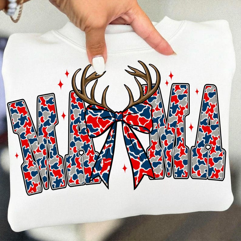 Peut inclure: Sweat-shirt blanc avec le mot "MAMA" en motif camouflage rouge, blanc et bleu. Un n&oelig;ud en forme de bois de cerf marron est centr&eacute; au-dessus du mot "MAMA". Des &eacute;clats d'&eacute;toiles rouges sont de chaque c&ocirc;t&eacute; du mot.