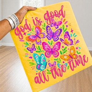 Peut inclure: Une couverture jaune avec un motif de papillons color&eacute;s et l'inscription rose "God is good all the time". Les papillons sont dans des tons de rose, violet, orange et turquoise.