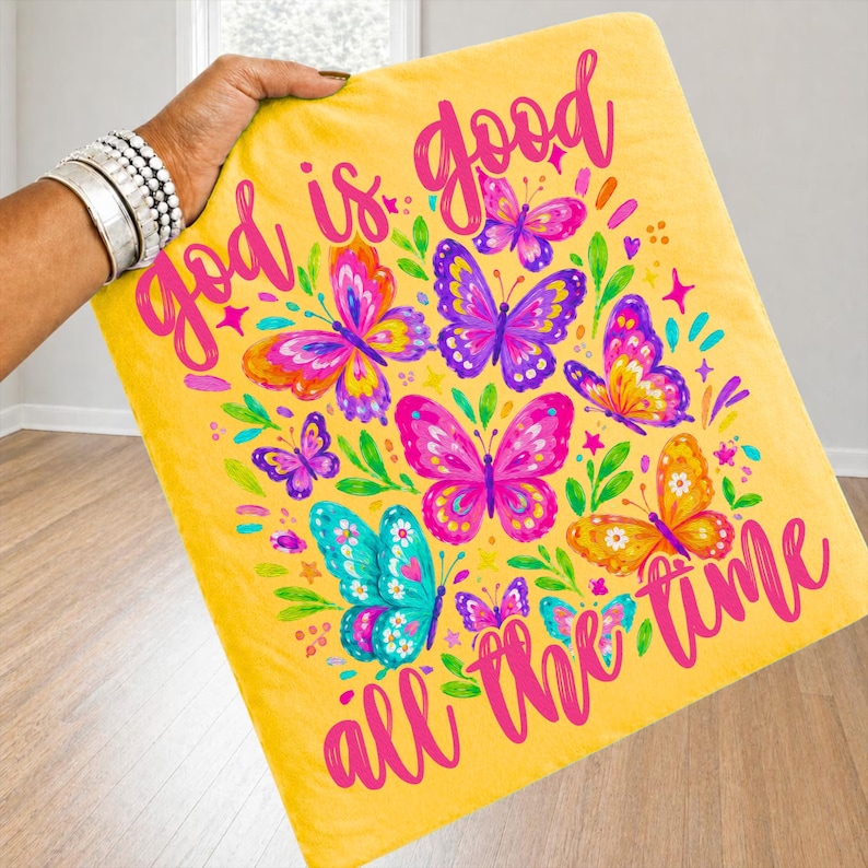 Peut inclure: Une couverture jaune avec un motif de papillons color&eacute;s et l'inscription rose "God is good all the time". Les papillons sont dans des tons de rose, violet, orange et turquoise.