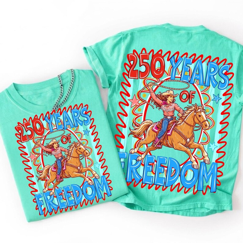 May include: Two turquoise t-shirts with a graphic design. The design features a cowgirl riding a horse with a lasso, surrounded by the text "250 YEARS OF FREEDOM" in red and blue. The shirts are made of a soft material.