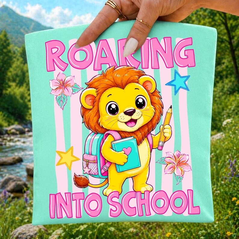 May include: A light mint green fabric square featuring a cartoon lion with a brown mane, wearing a pink backpack, holding a blue book and a yellow pencil. The text ROARING INTO SCHOOL is printed in pink. Pink vertical stripes decorate the background.