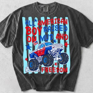 K&ouml;nnte beinhalten: Dunkelgraues T-Shirt mit einem Grafikdesign eines rot, wei&szlig; und blau gef&auml;rbten Monster Trucks und dem Text "ALL AMERICAN BOY RAISED ON MUD AND FREEDOM". Das Design beinhaltet Sterne und eine kleine amerikanische Flagge.