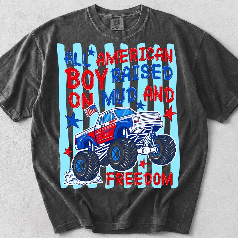 K&ouml;nnte beinhalten: Dunkelgraues T-Shirt mit einem Grafikdesign eines rot, wei&szlig; und blau gef&auml;rbten Monster Trucks und dem Text "ALL AMERICAN BOY RAISED ON MUD AND FREEDOM". Das Design beinhaltet Sterne und eine kleine amerikanische Flagge.