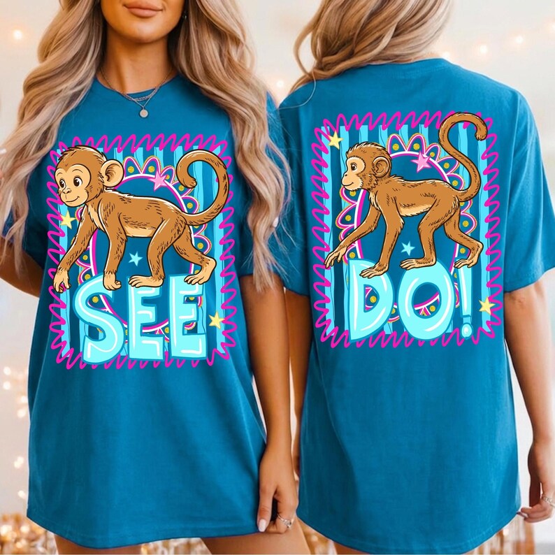 May include: Teal t-shirt featuring a brown monkey graphic with the words "SEE" and "DO!" in a light blue font. The monkey is inside a pink and blue frame with stars. The shirt has a relaxed fit.