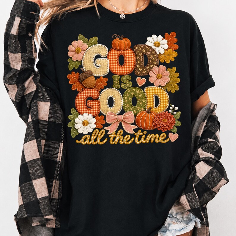 Pu&ograve; includere: Una t-shirt nera con una grafica che riporta il testo "GOD IS GOOD all the time" in un carattere decorativo. Il design include elementi a tema autunnale come zucche, ghiande, foglie autunnali, fiori, un fiocco e cuori in toni caldi.