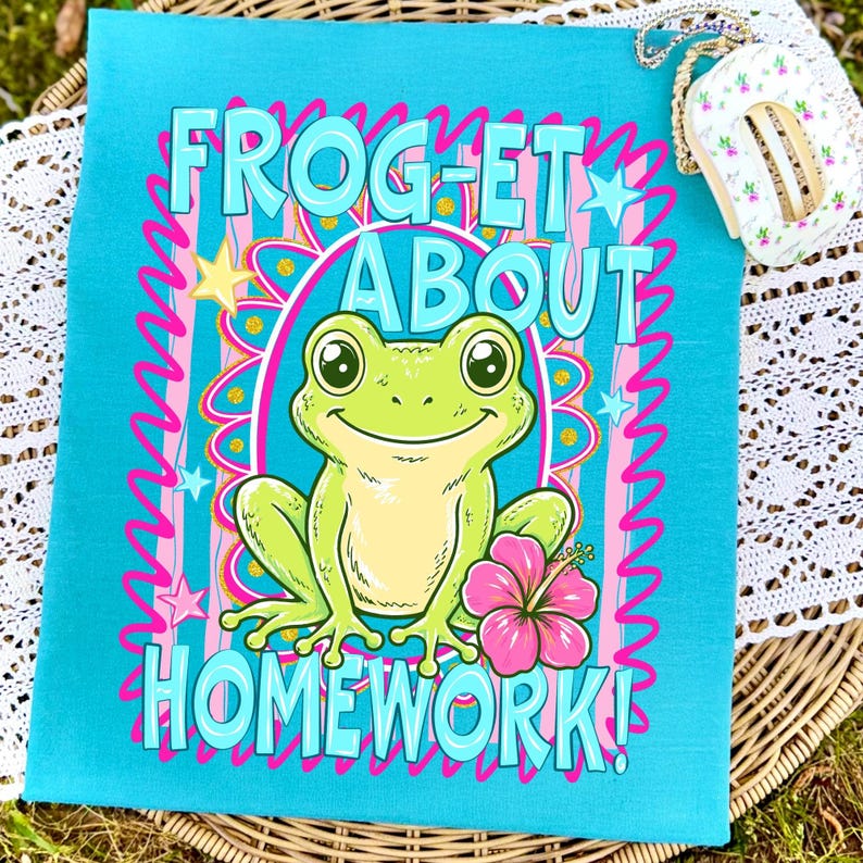 K&ouml;nnte beinhalten: T&uuml;rkisfarbenes Handtuch mit dem Schriftzug "FROG-ET ABOUT HOMEWORK!" in Hellblau. In der Mitte ist ein Cartoon-Frosch mit einer rosa Blume abgebildet. Das Design ist mit rosa und wei&szlig;en Wellenlinien und Sternen umrahmt.