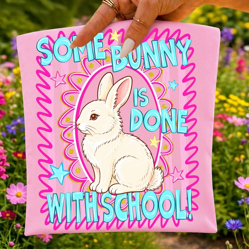 Może przedstawiać: R&oacute;żowa poduszka z napisem "SOME BUNNY IS DONE WITH SCHOOL!" w kolorze turkusowym. Biały kr&oacute;lik jest wyśrodkowany w r&oacute;żowym owalu. Projekt zawiera gwiazdy i ozdobną obw&oacute;dkę.