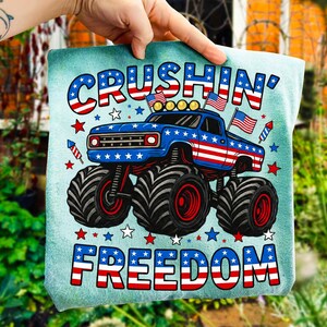 K&ouml;nnte beinhalten: Eine t&uuml;rkisgr&uuml;ne Tragetasche mit einem patriotischen Monster-Truck-Design. Der Truck ist blau mit roten und wei&szlig;en Streifen und Sternen, und der Text "CRUSHIN' FREEDOM" ist in Rot, Wei&szlig; und Blau dargestellt. Die Tasche wird von einer Hand gehalten.