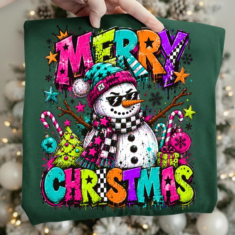 Puede incluir: Una sudadera verde oscuro con un gr&aacute;fico de un mu&ntilde;eco de nieve con gafas de sol, un gorro azul verdoso y una bufanda a cuadros blancos y negros. El texto MERRY CHRISTMAS est&aacute; impreso en letras grandes y coloridas de estilo grafiti.