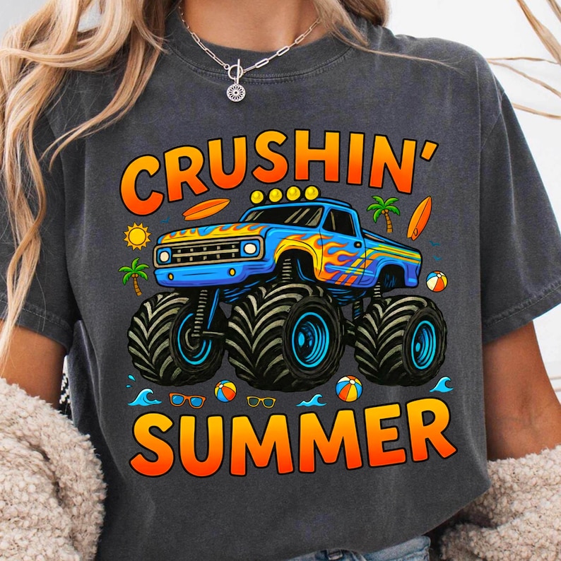 May include: Dark gray t-shirt featuring a blue monster truck with orange and yellow flames, the words "CRUSHIN' SUMMER" in orange and yellow, and summer-themed graphics like surfboards, palm trees, and beach balls.