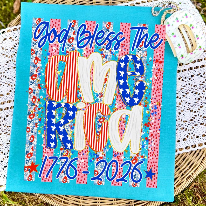 Puede incluir: Un cuadrado de tela turquesa con las palabras "God Bless The America" en escritura azul. La palabra "America" est&aacute; en rojo, blanco y azul con un estampado floral. Los n&uacute;meros "1776-2026" est&aacute;n en la parte inferior.
