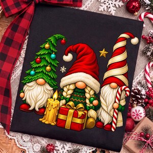 Puede incluir: Una camiseta negra con un gr&aacute;fico de tres gnomos. Un gnomo tiene forma de &aacute;rbol de Navidad verde con adornos, otro tiene trenzas rubias y un gorro rojo, y el tercero lleva un gorro de rayas rojas y blancas mientras sostiene un bast&oacute;n de caramelo.