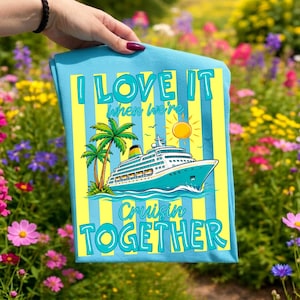 May include: A light blue t-shirt with a cruise ship graphic, palm trees, and the text "I LOVE IT when we're Cruisin TOGETHER". The design features yellow and blue vertical stripes and a sun.