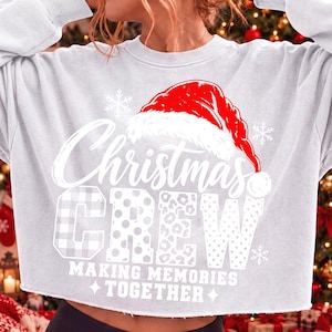 May include: A light gray long-sleeve sweatshirt featuring a red Santa hat graphic above the white text Christmas CREW. The letters in CREW have varied patterns including plaid, polka dots, and leopard print. Below is the text MAKING MEMORIES TOGETHER.