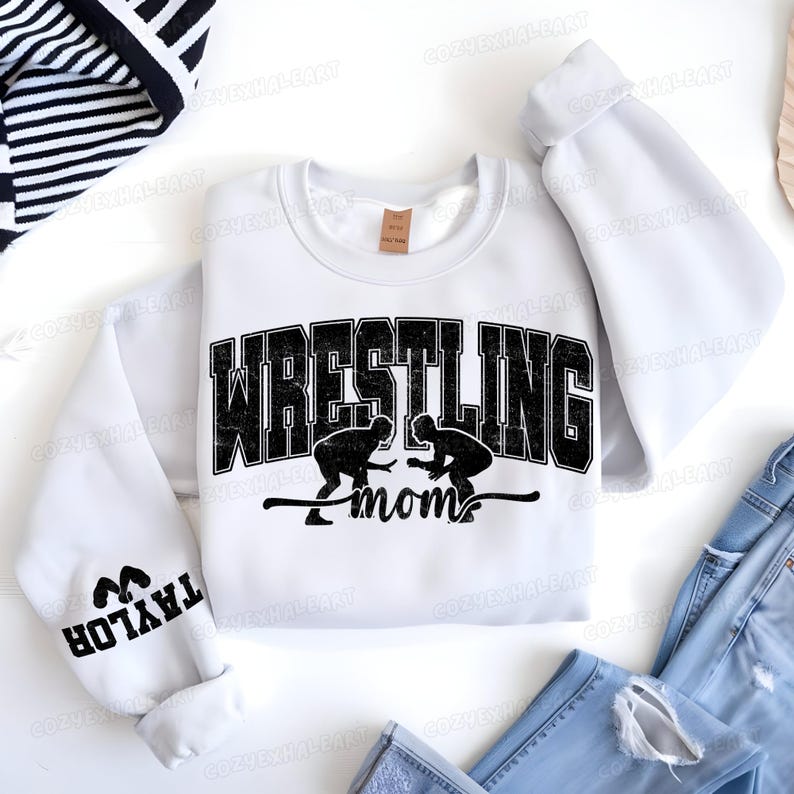 May include: White sweatshirt with the word "WRESTLING" in large, black, distressed lettering. Below the word is the word "mom" and two wrestling figures. The left sleeve has the name "TAYLOR" in black.
