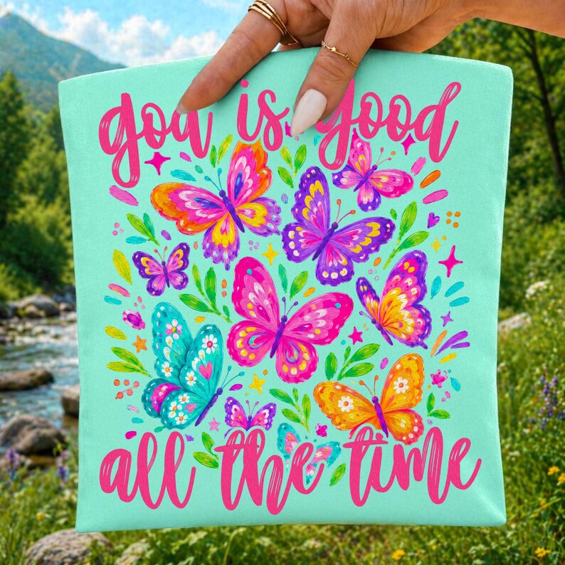 May include: A light mint green fabric square featuring the pink cursive text "god is good all the time" and a colorful illustration of multiple butterflies in shades of pink, purple, yellow, and blue, accented with small green leaves and stars.