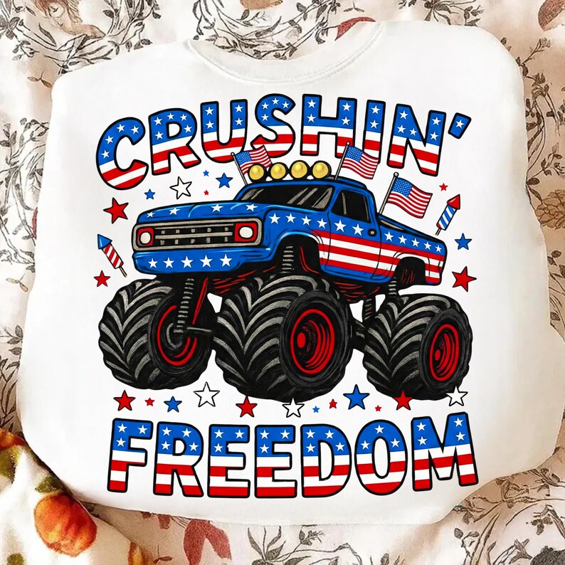 K&ouml;nnte beinhalten: Wei&szlig;es Sweatshirt mit patriotischem Design. Es zeigt einen blauen Monstertruck mit roten und wei&szlig;en Akzenten, amerikanische Flaggen und die Worte "Crushin' Freedom" in Rot, Wei&szlig; und Blau.