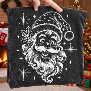 May include: A dark charcoal gray fabric featuring a white line art illustration of a smiling Santa Claus wearing a hat with polka dots. The design includes a sprig of holly with berries and several four-pointed starbursts scattered around the face.