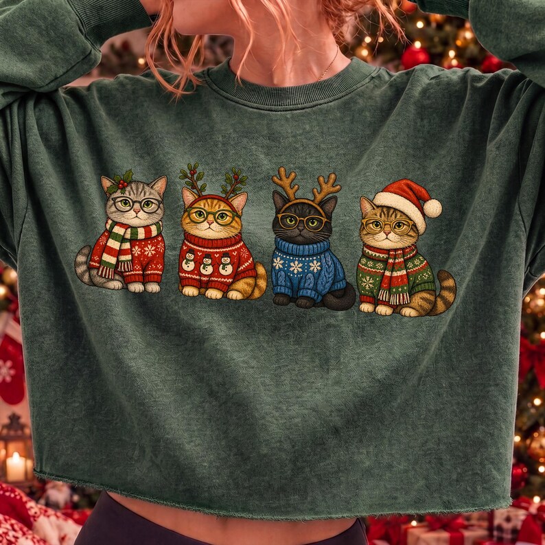 K&ouml;nnte beinhalten: Ein dunkelgr&uuml;nes Langarm-Sweatshirt mit einem Grafikdruck von vier Katzen in festlicher Kleidung. Die Katzen sind mit Brillen, Schals, Pullovern mit Schneemannmustern und weihnachtlichen Kopfbedeckungen wie Rentiergeweihen und einer Weihnachtsm&uuml;tze abgebildet.