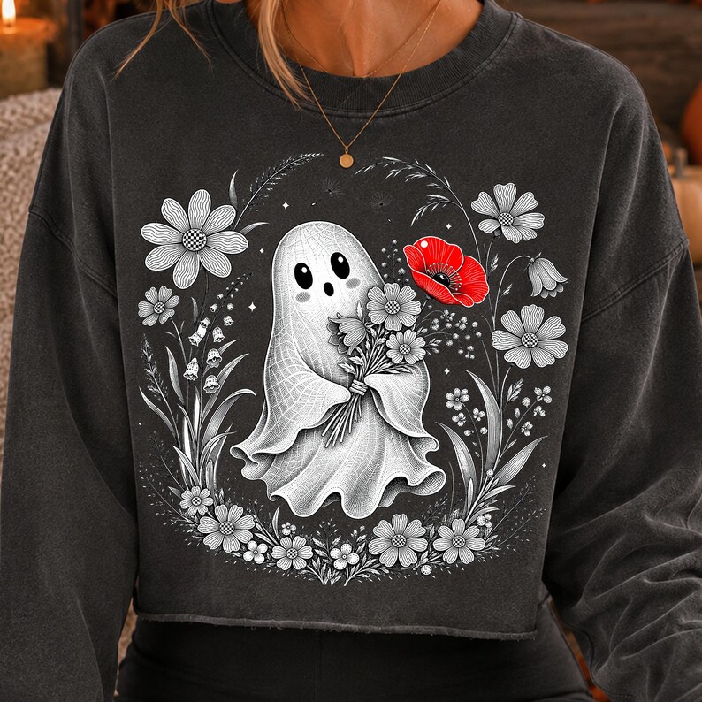 K&ouml;nnte beinhalten: Ein anthrazitfarbenes Sweatshirt mit Rundhalsausschnitt und einem Grafikdruck eines wei&szlig;en Geistes, der einen Blumenstrau&szlig; h&auml;lt. Das Design zeigt schwarz-wei&szlig;e Strichzeichnungen von Blumen um den Geist herum, mit einer leuchtend roten Mohnblume.