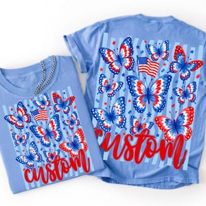 Peut inclure: Un t-shirt bleu clair avec un imprim&eacute; graphique de papillons rouges, blancs et bleus, un drapeau am&eacute;ricain et de petites &eacute;toiles sur des rayures verticales. Le mot "custom" est imprim&eacute; en &eacute;criture rouge au bas du motif graphique.