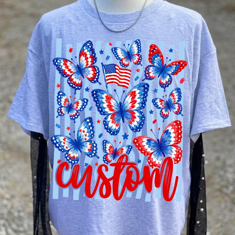 Peut inclure: Un t-shirt gris clair &agrave; manches courtes avec une impression graphique de plusieurs papillons aux motifs rouges, blancs et bleus. Un petit drapeau am&eacute;ricain est plac&eacute; parmi les papillons et le mot custom est &eacute;crit en &eacute;criture rouge en bas.