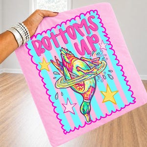 May include: Pink blanket featuring a cartoon duck illustration and the words "BOTTOMS UP" in pink. The duck is colourful with a ring around it, and there are stars and water droplets. The blanket is held up by a person.