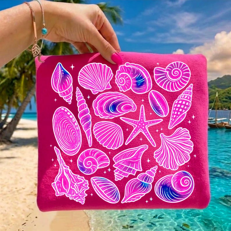 Pu&ograve; includere: Una pochette con cerniera rosa acceso con illustrazioni di conchiglie bianche e rosa. La pochette &egrave; tenuta contro una scena di spiaggia tropicale con palme, acqua blu e cielo sereno.