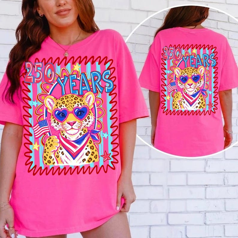 Op de afbeelding: Felroze t-shirt met een luipaard met een hartvormige zonnebril en een patriottische bandana, met een Amerikaanse vlag. Het shirt heeft de tekst "250 YEARS" in een kleurrijk ontwerp. De achterkant van het shirt heeft ook hetzelfde ontwerp.