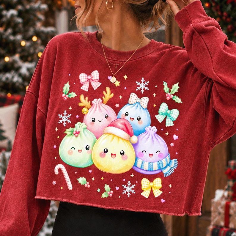 May include: A dark red long-sleeve cropped sweatshirt featuring a graphic print of five colourful, smiling dumpling characters. The central dumpling wears a red Santa hat, while others are decorated with reindeer antlers, a blue scarf, and bows.