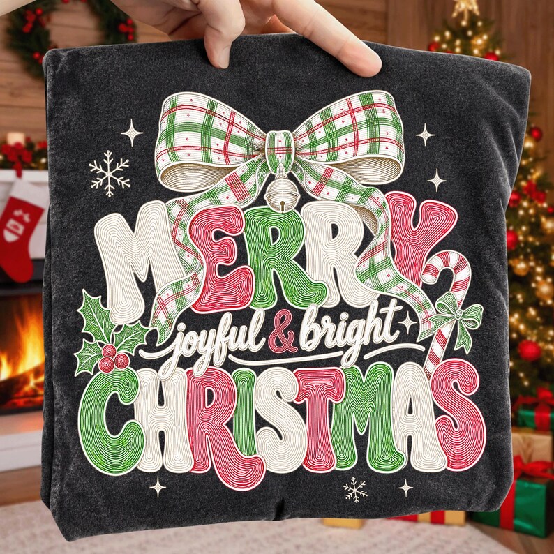 K&ouml;nnte beinhalten: Ein dunkelgraues Sweatshirt mit einem gro&szlig;en Aufdruck, der oben eine gr&uuml;n-rote karierte Schleife zeigt. Der Text Merry joyful & bright Christmas ist in stilisierter, texturierter Schrift gehalten. Das Design enth&auml;lt Stechpalmen, Beeren und eine Zuckerstange.