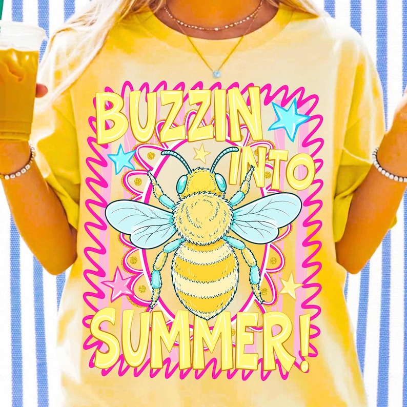 K&ouml;nnte beinhalten: Gelbes T-Shirt mit einem gro&szlig;en Bienen-Motiv und dem Schriftzug "Buzzin' Into Summer!". Die Biene ist gelb und schwarz mit blauen Fl&uuml;geln, umgeben von Sternen und einem rosa Rand. Der Text ist in einer verspielten Schriftart.