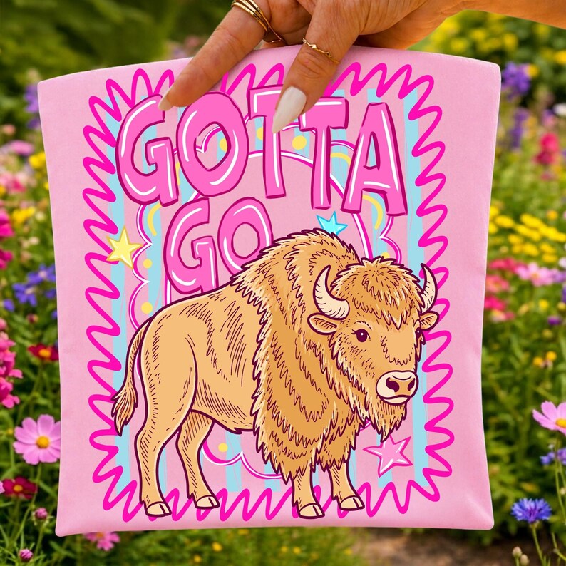 May include: Pink t-shirt featuring a cartoon bison illustration with the text "GOTTA GO" in pink bubble letters. The bison is tan with a shaggy mane and horns. The design includes stars and a wavy pink border.