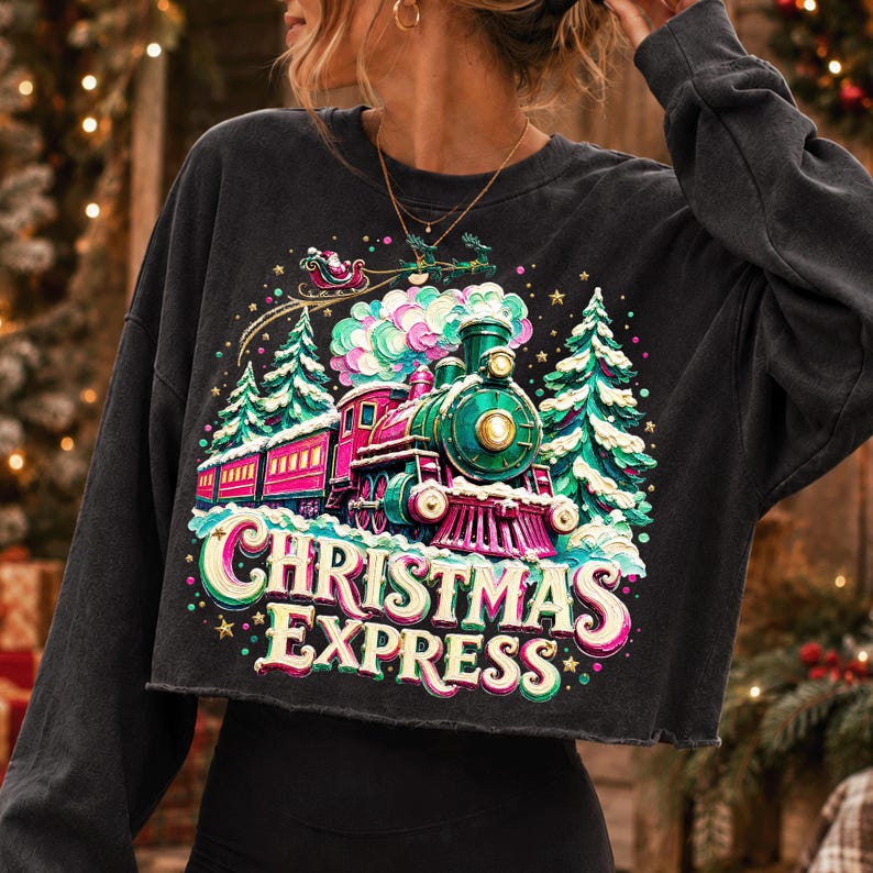 May include: A charcoal grey long-sleeve cropped sweatshirt featuring a colourful graphic of a steam train, evergreen trees, and a flying sleigh. The text "CHRISTMAS EXPRESS" is printed in large, stylised lettering below the train illustration.