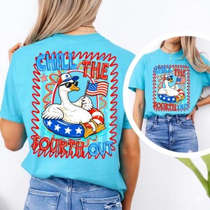 Peut inclure: T-shirt bleu clair avec un dessin d'oie de dessin anim&eacute; portant des lunettes de soleil et un chapeau patriotique, flottant sur une bou&eacute;e rouge, blanche et bleue. Le t-shirt porte l'inscription "Chill the Fourth Out", parfait pour le 4 juillet.
