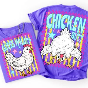 May include: Two purple t-shirts with chicken-themed graphics. One shirt says "Guess What?" with a cartoon chicken. The other says "Chicken Butt" with a chicken bending over. Both shirts have colorful star and line accents.