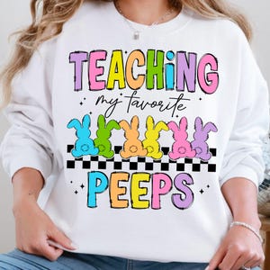 May include: White sweatshirt with the text "TEACHING my favourite PEEPS" in rainbow colours. There are six colourful cartoon chicks in a row below the text.