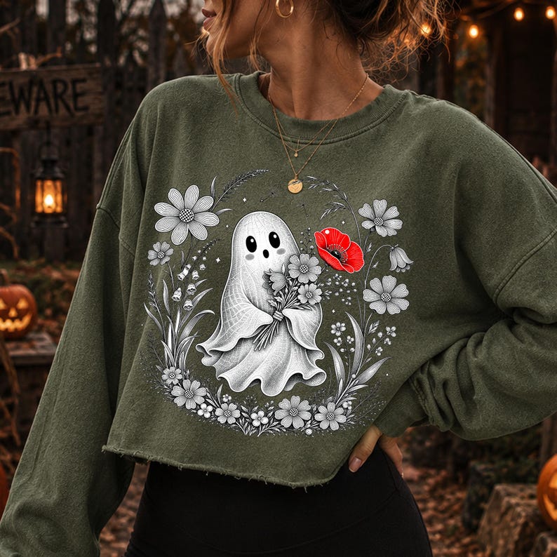 K&ouml;nnte beinhalten: Ein olivgr&uuml;nes Langarm-Sweatshirt mit einem Grafikdruck eines wei&szlig;en Geistes, der einen Blumenstrau&szlig; h&auml;lt. Das Design zeigt eine kreisf&ouml;rmige Anordnung von schwarz-wei&szlig;en Strichzeichnungen von Blumen mit einer einzelnen leuchtend roten Mohnblume.